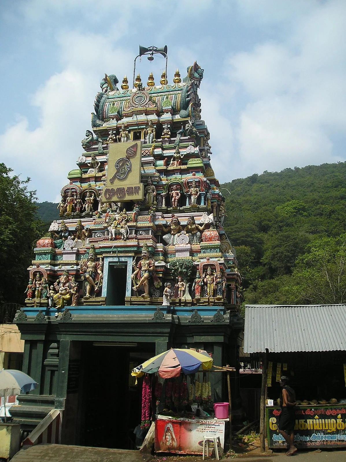 The colourful entrance tower of Pazhamudircholai Murugan Temple below a green hill